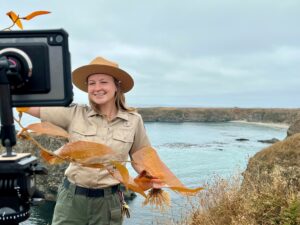 Program presenter holding a strand of kelp with the ocean in the background